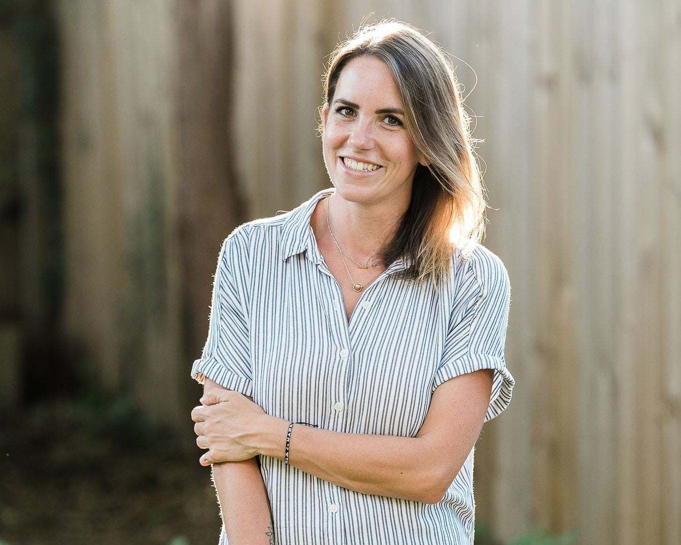 Woman standing outdoors with a wooden fence and greenery in the background